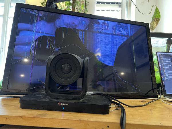 A TV set with visibly broken LCD panel and the camera next to it. An image is visible on the TV, the top left shows a face looking into the camera, while other parts of the screen are glitched or even off. One last movie